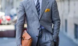 Uomo con completo grigio in lino, camicia azzurra e cravatta azzurra a righe. Un perfetto cravatta azzurra abbinamento con pochette gialla.