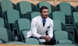 David Beckham in una giacca bianca uomo abbinamento impeccabile, con camicia azzurra e cravatta blu, siede tra le tribune verdi di Wimbledon.