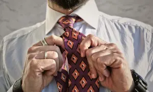 Uomo che sistema il nodo cravatta Eldredge, con camicia bianca e cravatta a rombi arancioni e viola.