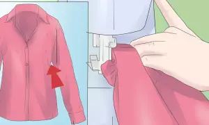 Mani che guidano una maglietta rosa sotto una macchina da cucire, con un'immagine ingrandita della maglietta che mostra una freccia rossa. Impara come restringere una maglietta.