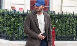 Uomo con abbinamento blu e marrone: blazer marrone, t-shirt bianca, cappellino blu e pantaloni scuri.