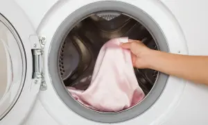 Mano inserisce un capo colorato in lavatrice. Ecco come lavare i capi colorati la prima volta per evitare che stingano.