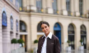 Donna con outfit camicia bianca inverno, giacca marrone e sfondo di un edificio parigino.