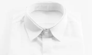 Primo piano di una camicia bianca da uomo, con colletto ben definito e abbottonatura maschile impeccabile.