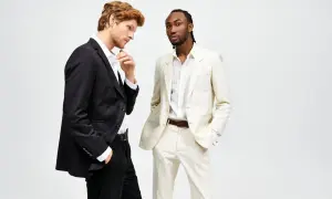 Due uomini in abiti eleganti. Uno con giacca nera e pantaloni neri, l'altro con giacca e pantaloni color crema. Il **regular fit significato** è un taglio classico e confortevole.