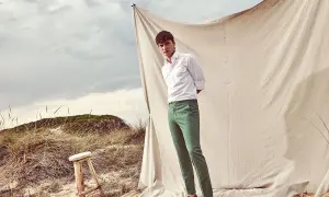 Uomo con camicia bianca e abbinamento pantalone verde su sfondo naturale.