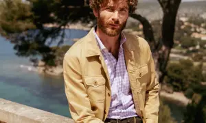 Uomo con camicia a quadri viola e giacca color sabbia, un'idea di cosa mettere sopra una camicia per un look casual chic.