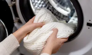 Mani che inseriscono un maglione bianco nella lavatrice. Speriamo che la lavatrice non lava bene i bianchi, altrimenti questo capo rimarrà grigio.