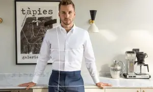 Uomo in camicia bianca e pantaloni blu, con linee bianche sovrapposte che indicano come arrotolare le maniche della camicia.