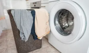 Cesto della biancheria con capi grigi e beige accanto a una lavatrice. Come risolvere quando un capo perde colore?