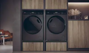 Due asciugatrici nere affiancate, con un cassetto in legno sotto ciascuna. Le lenzuola in asciugatrice sono pronte per essere piegate.