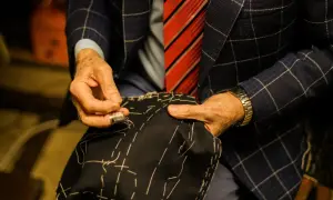 Sarto esperto cuce a mano un tessuto scuro, mostrando i diversi tipi di polsini camicia e la cura artigianale.