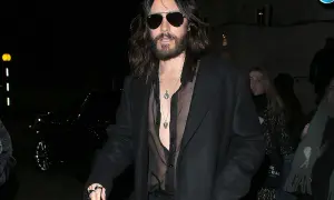 Jared Leto con un audace outfit camicia nera trasparente sotto un cappotto scuro, collane d'argento e occhiali da sole.