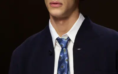Primo piano di un uomo con un elegante nodo cravatta matrimonio, indossa una camicia bianca e una giacca blu scuro.