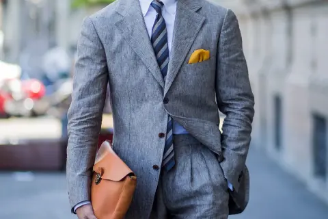 Uomo con completo grigio in lino, camicia azzurra e cravatta azzurra a righe. Un perfetto cravatta azzurra abbinamento con pochette gialla.
