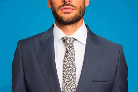 Uomo con abito grigio, camicia bianca e cravatta fantasia. L'abbinamento camicia cravatta è curato nei minimi dettagli.
