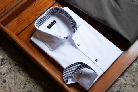 Camicia bianca da uomo con colletto e doppio polsino a quadri marroni e neri, pronta per un'occasione speciale.