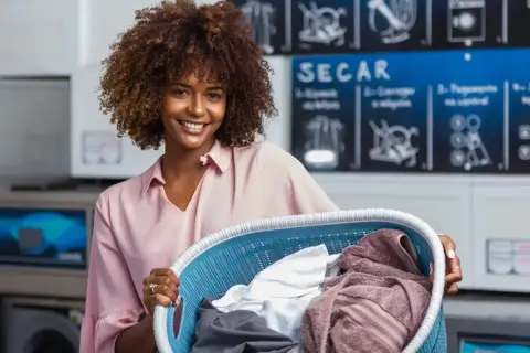 Donna sorridente con un cesto di panni in lavanderia. Attenzione, la centrifuga restringe i capi se non si usa il programma giusto!