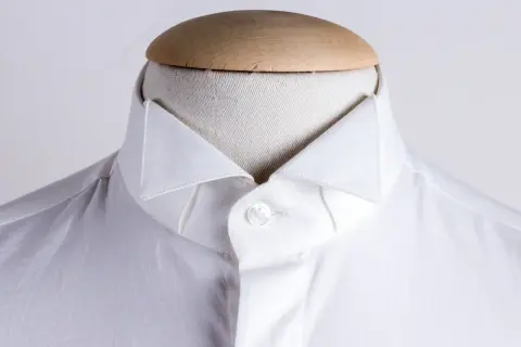 Dettaglio di una camicia bianca da uomo con un elegante camicia con colletto a punta, abbottonata su un manichino.