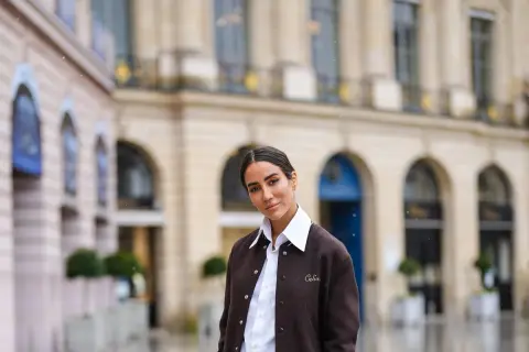 Donna con outfit camicia bianca inverno, giacca marrone e sfondo di un edificio parigino.