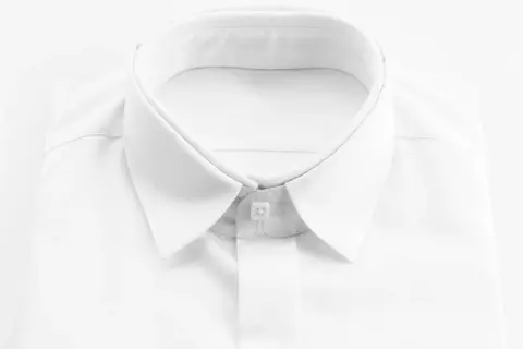 Primo piano di una camicia bianca da uomo, con colletto ben definito e abbottonatura maschile impeccabile.
