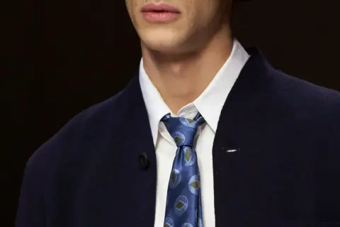 Primo piano di un uomo con un elegante nodo cravatta matrimonio, indossa una camicia bianca e una giacca blu scuro.