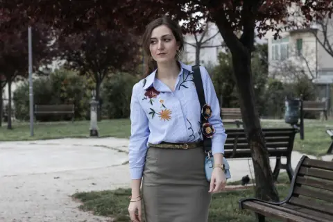 Donna con camicie ricamate a fiori, in un parco con panchine e alberi.