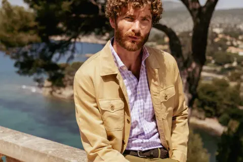 Uomo con camicia a quadri viola e giacca color sabbia, un'idea di cosa mettere sopra una camicia per un look casual chic.