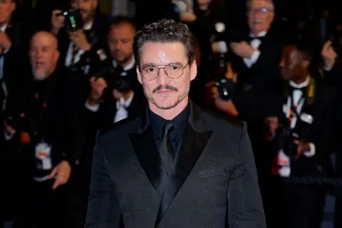 Pedro Pascal sfoggia un impeccabile outfit giacca nera uomo, con camicia e cravatta abbinate, occhiali da vista e baffi.