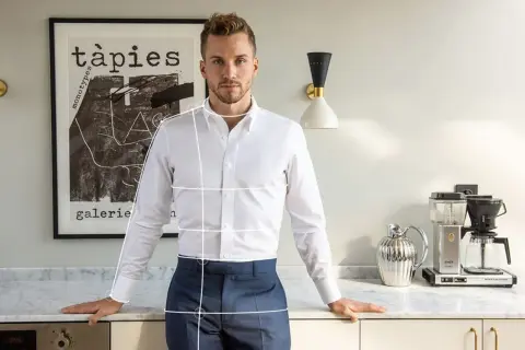 Uomo in camicia bianca e pantaloni blu, con linee bianche sovrapposte che indicano come arrotolare le maniche della camicia.