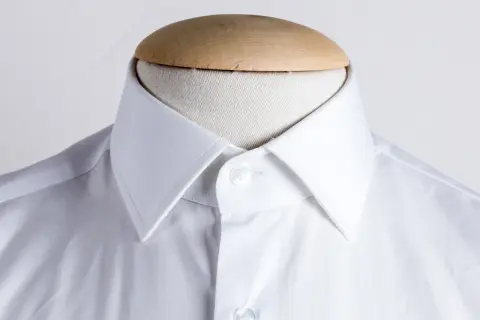 Dettaglio di una camicia bianca con collo italiano, pronta per essere indossata.