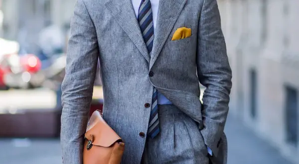 Uomo con completo grigio in lino, camicia azzurra e cravatta azzurra a righe. Un perfetto cravatta azzurra abbinamento con pochette gialla.