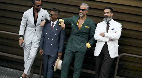 Quattro uomini eleganti in abiti sartoriali. Il completo beige e nero stanno bene insieme, creando un look sofisticato.