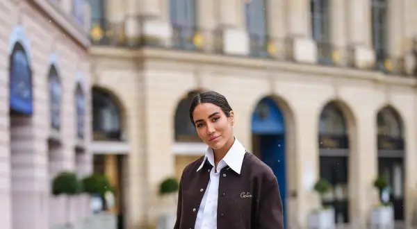 Donna con outfit camicia bianca inverno, giacca marrone e sfondo di un edificio parigino.
