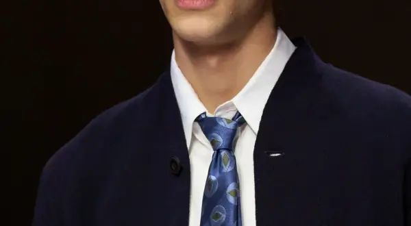 Primo piano di un uomo con un elegante nodo cravatta matrimonio, indossa una camicia bianca e una giacca blu scuro.