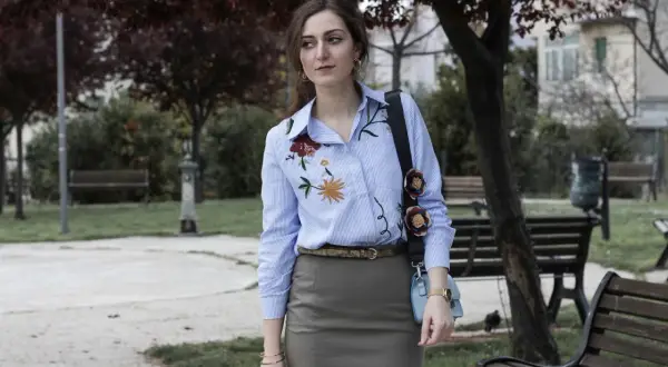 Donna con camicie ricamate a fiori, in un parco con panchine e alberi.