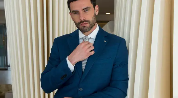 Uomo in abito blu che sistema la cravatta, un esempio di come si mette cravatta con stile.