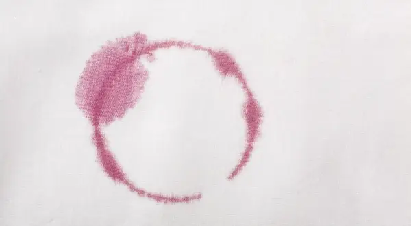 Macchie rosse sui vestiti dopo lavaggio in lavatrice, un alone circolare di vino su tessuto bianco.