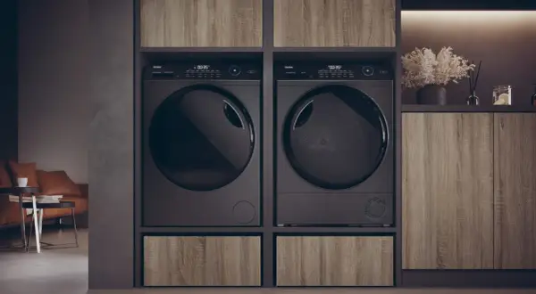Due asciugatrici nere affiancate, con un cassetto in legno sotto ciascuna. Le lenzuola in asciugatrice sono pronte per essere piegate.