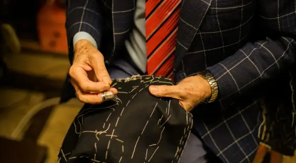 Sarto esperto cuce a mano un tessuto scuro, mostrando i diversi tipi di polsini camicia e la cura artigianale.