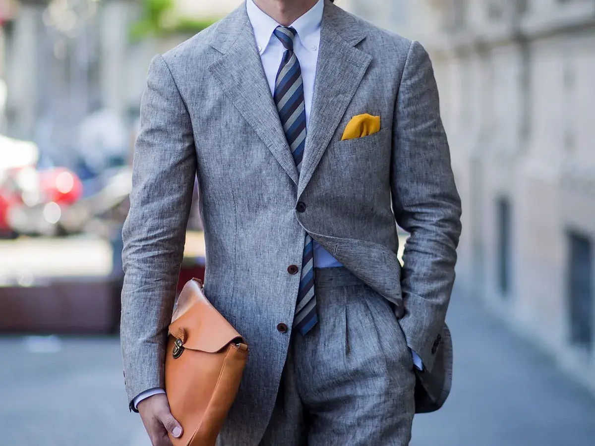 Uomo con completo grigio in lino, camicia azzurra e cravatta azzurra a righe. Un perfetto cravatta azzurra abbinamento con pochette gialla.