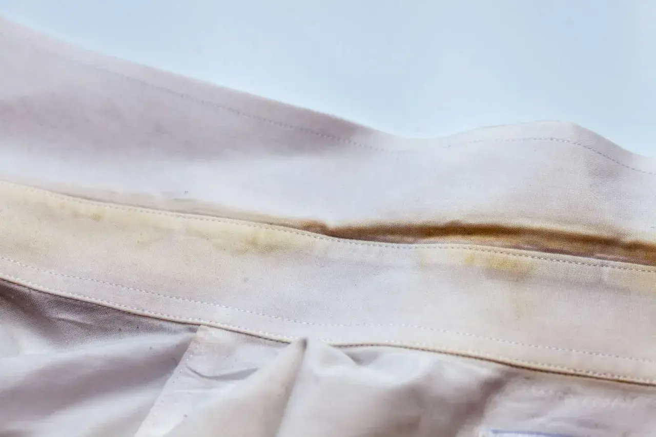 Colletto di camicia con evidenti macchie gialle, simili a quelle che si formano su asciugamani colorati dopo l'uso.