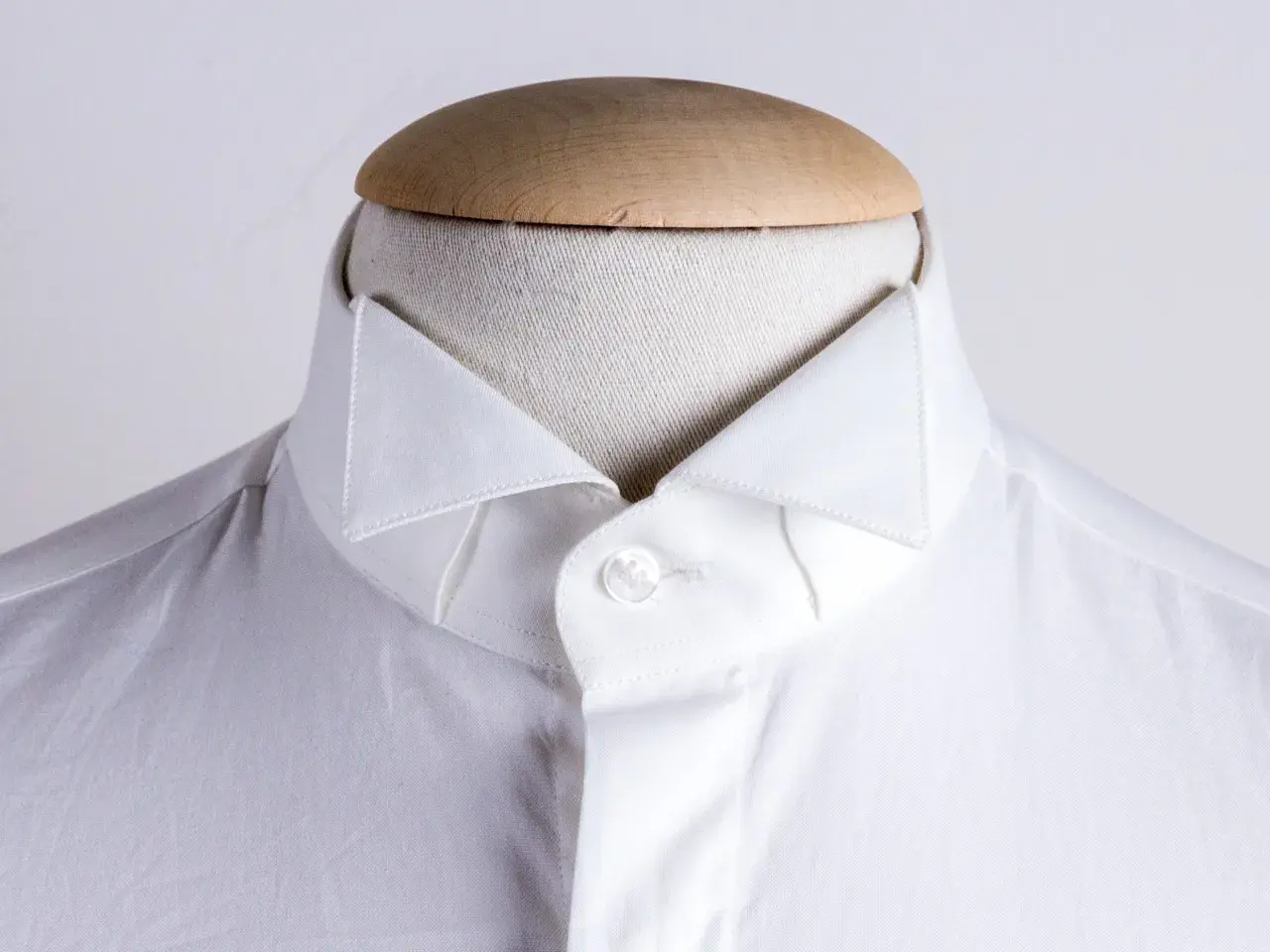 Dettaglio di una camicia bianca da uomo con un elegante camicia con colletto a punta, abbottonata su un manichino.