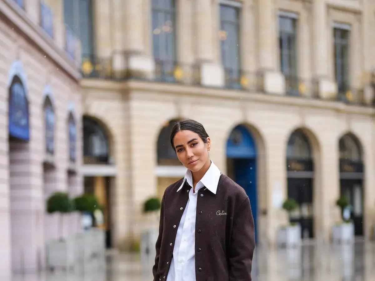 Donna con outfit camicia bianca inverno, giacca marrone e sfondo di un edificio parigino.