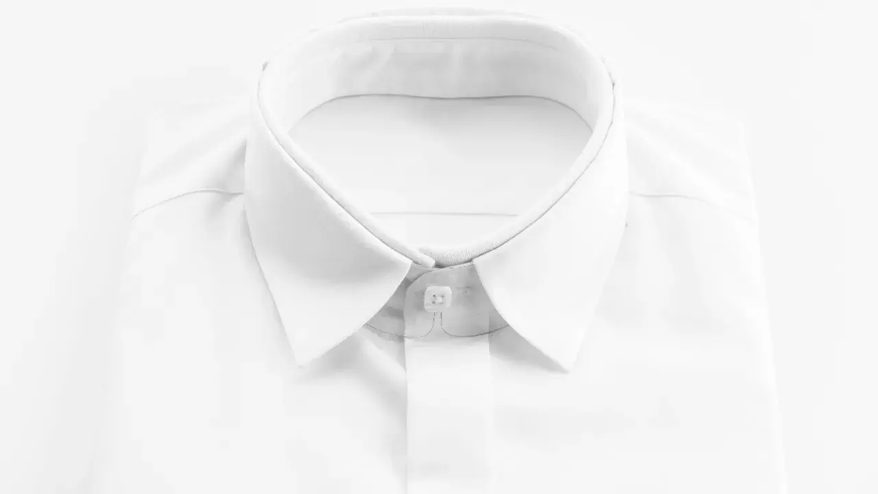 Primo piano di una camicia bianca da uomo, con colletto ben definito e abbottonatura maschile impeccabile.