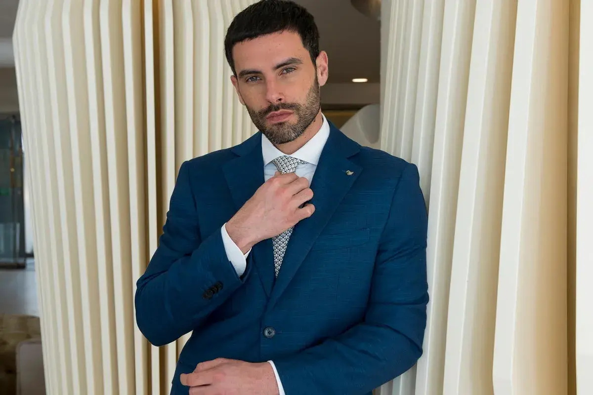 Uomo in abito blu che sistema la cravatta, un esempio di come si mette cravatta con stile.