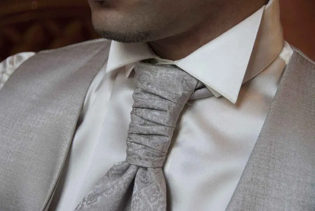 Primo piano di un uomo con un elegante nodo cravatta grigio su camicia bianca e gilet coordinato.