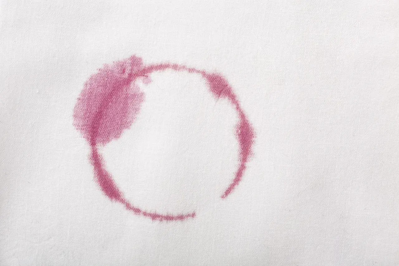 Macchie rosse sui vestiti dopo lavaggio in lavatrice, un alone circolare di vino su tessuto bianco.