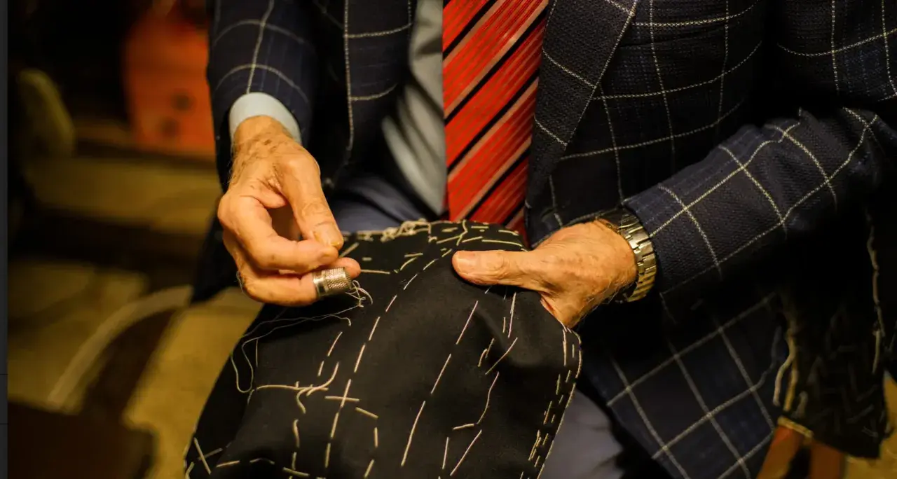 Sarto esperto cuce a mano un tessuto scuro, mostrando i diversi tipi di polsini camicia e la cura artigianale.