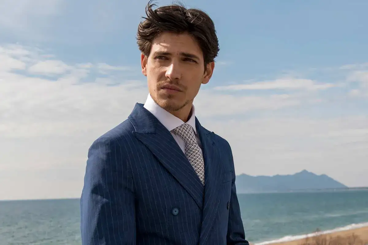 Uomo con abito blu gessato e cravatta con fantasia geometrica, pronto per un matrimonio. Il nodo cravatta matrimonio &egrave; perfetto.